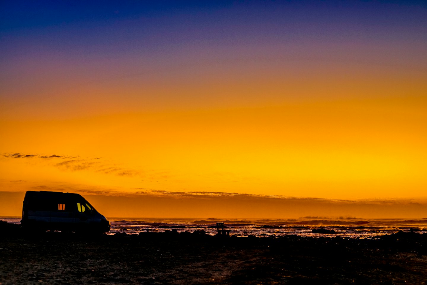 Bobil parkert på en strand ved solnedgang.