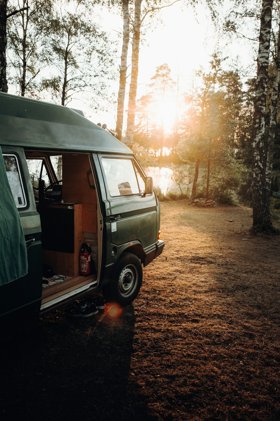 Mørkegrønn campingbil parkert med åpen dør ved solnedgang.